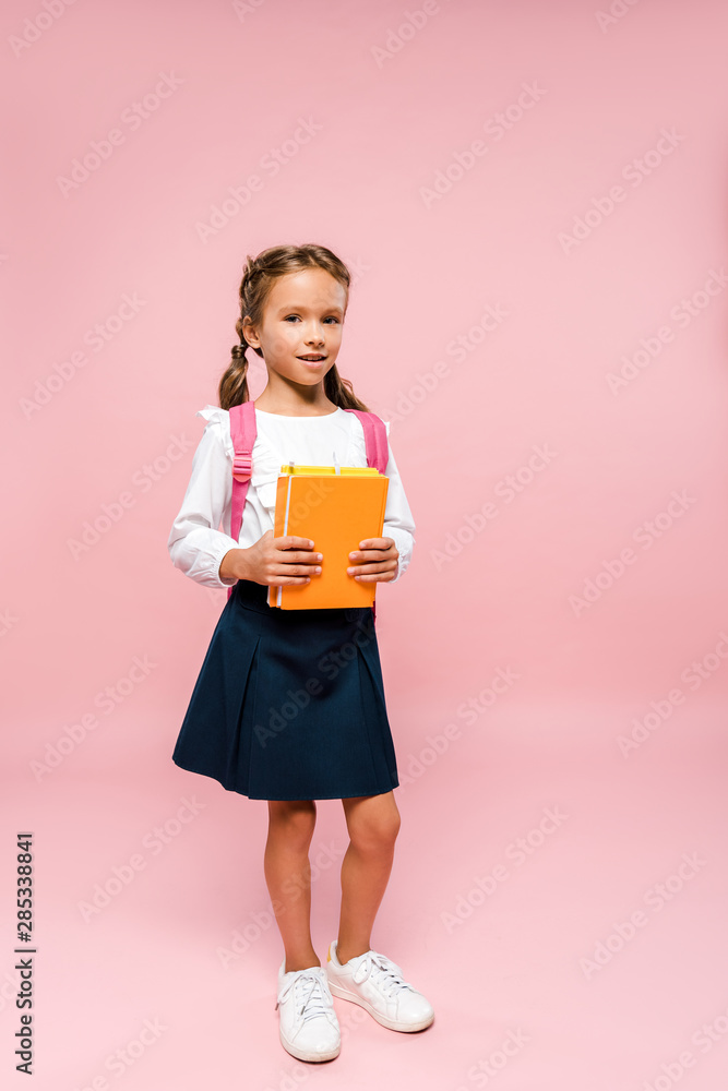 happy kid holding books while standing with backpack on pink happy kid holding books while standing with backpack on pink
