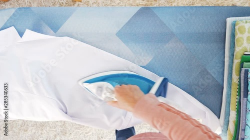 Female hands ironing clothes with iron on ironing board