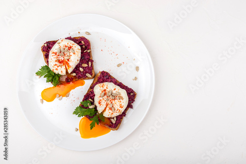Poached eggs with homemade beetroot hummus, seeds and parsley on toast bread on a white plate on the white background. Healthy breakfast or snack. Copy space