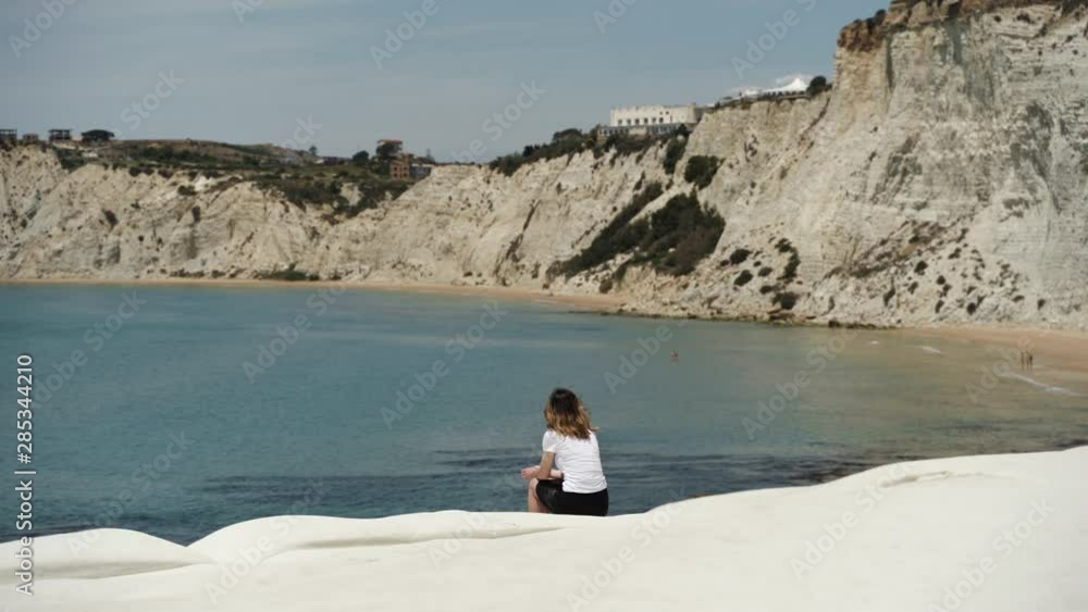 Woman sitting on white rock cliff Scala dei Turchi by sea coastline in Sicily Woman sitting on white rock cliff Scala dei Turchi by sea coastline in Sicily