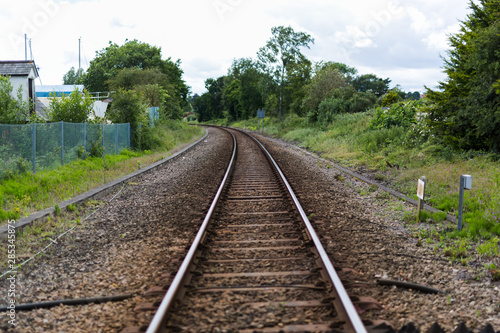 A single set of train tracks leading to a vanishing point on the horizon, the train line is cutting through rural british countryside