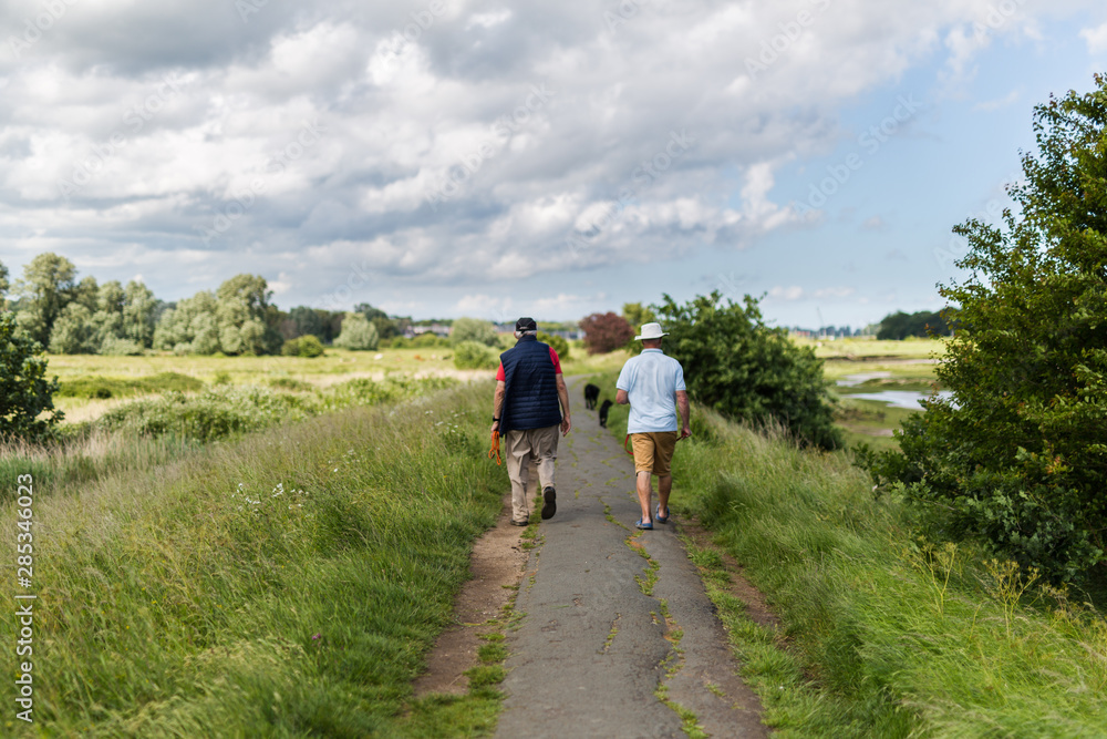 2 middle aged male's walking their dogs along a popular river path