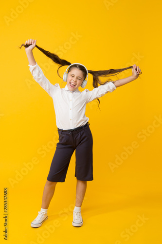 Grow hair with music. Small child wearing long tail hairstyle and headphones for school. Little girl holding hairstyle on yellow background. Cute kid enjoying music and her hairstyle. Easy hairstyle photo