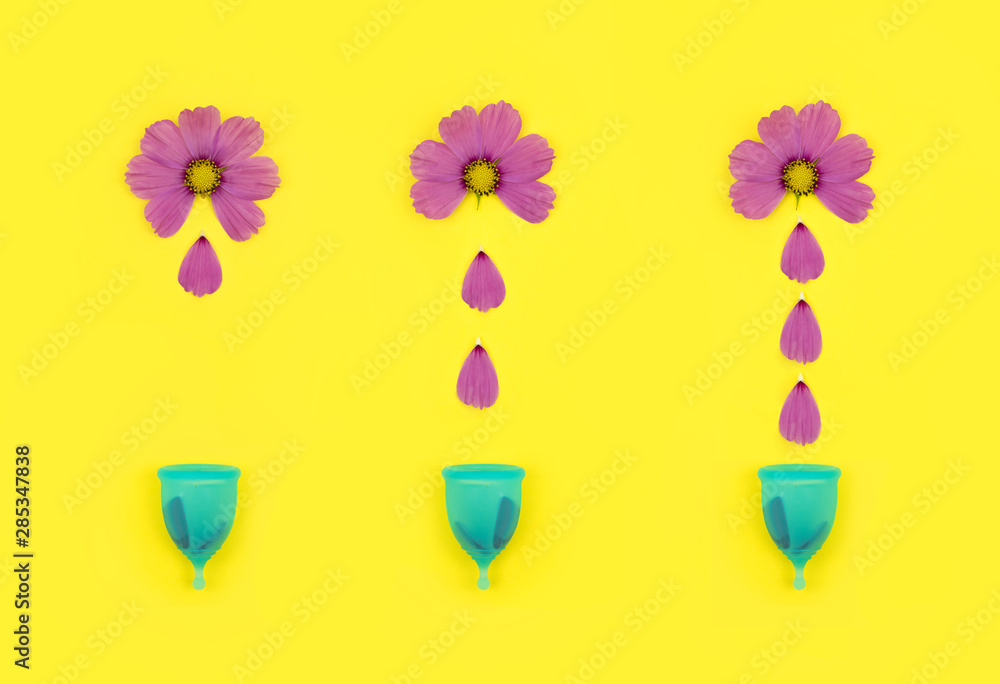 a pink flower on a yellow isolated background depicts bleeding in the period, the petals like drops of blood falling into a blue menstrual cup. demonstrations of personal intimate hygiene products for