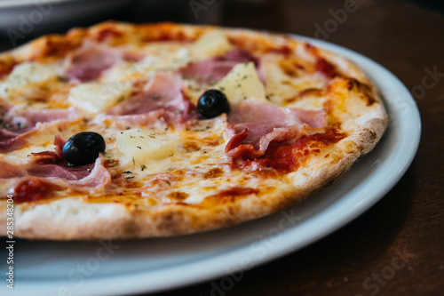 Delicious Pizza Hawaii with Olives served on a Plate in Pizzeria Restaurant