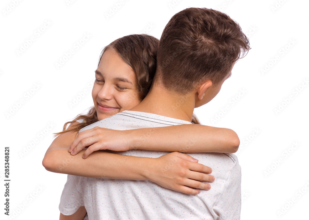 Sweet young couple in love. Happy teenagers standing together and hugging, isolated on white background. Teen girl hugging her boyfriend with eyes closed. Concept about love, people and lifestyle. Sweet young couple in love. Happy teenagers standing together and hugging, isolated on white background. Teen girl hugging her boyfriend with eyes closed. Concept about love, people and lifestyle.