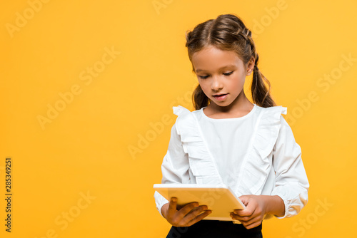 cute schoolchild with backpack holding book isolated on orange