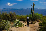 A desert hiker stops to admire a giant cactus and the Santa Catalina Mountains in Saguaro National Park, Arizona