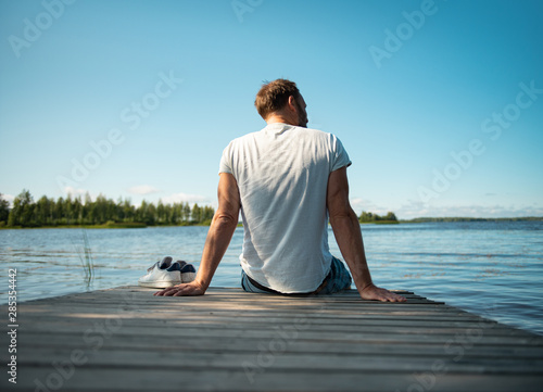 Mann sitzt auf Holzsteg am See in Finnland