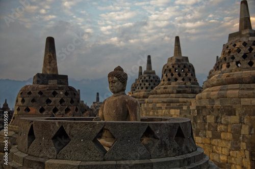 Java, Indonesia - July 24, 2019: Amazing sunrise view of meditating Buddha statue and stone stupas. Ancient Borobudur Buddhist temple. Great religious architecture