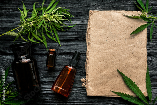 Cannabis cbd oil bottle, green leaves and blank page book with a copy space on a black background.