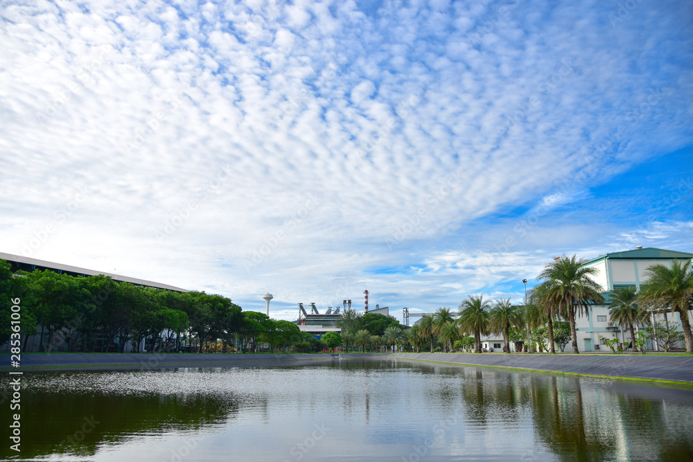 Obraz premium The pond is surrounded by trees and the factory. The background is blue sky and Cloud