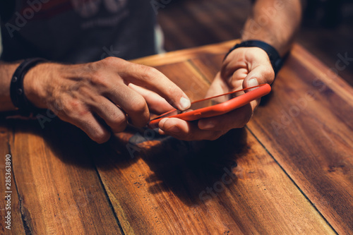 young guy with a beard in a shirt and headphones,Young and smiling man sitting on the roof with mobile phone and listening music (intentional sun glare and vintage color, focus on mobile phone