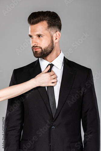 woman touching tie on successful businessman in black suit isolated on grey