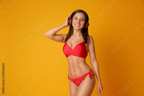 Pretty sexy woman with slim body in stylish red bikini and headphones on orange background, space for text
