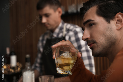 Young man with glass of whiskey in bar. Space for text