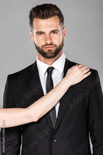 woman touching shoulder of successful businessman in black suit isolated on grey