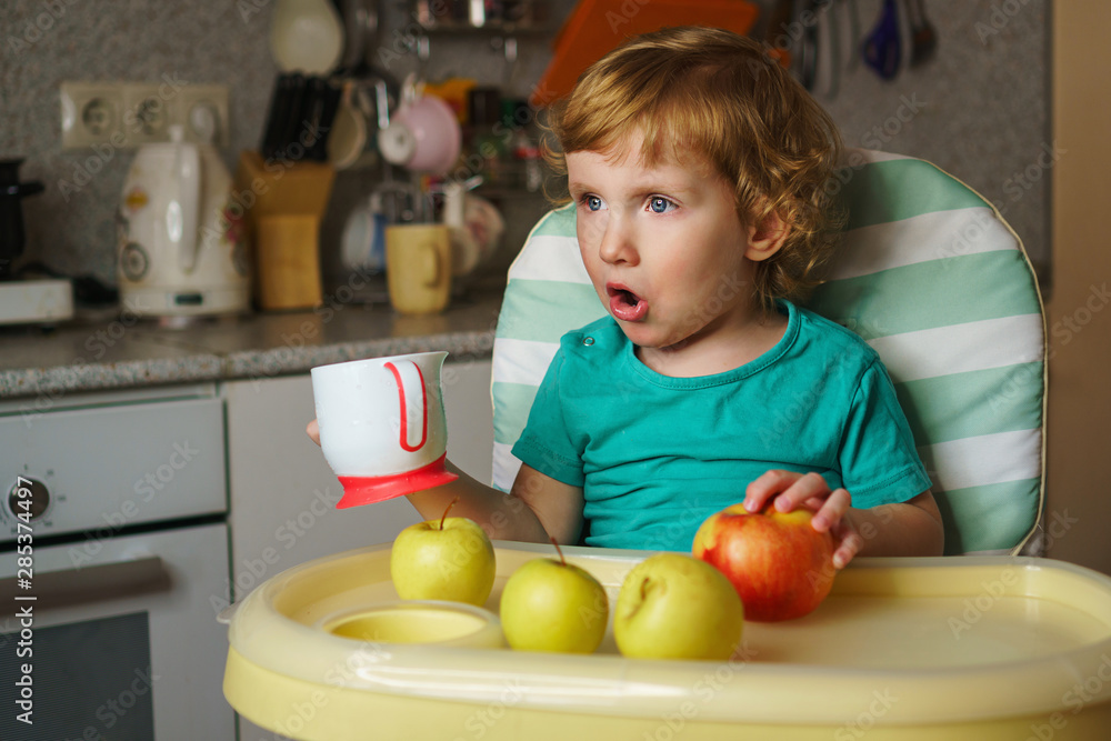 Charming little child eating in the kitchen. He sits in a highchair. Vegetables, fruits, healthy food. The concept of proper nutrition for health of baby. Boy needs a drink. Charming little child eating in the kitchen. He sits in a highchair. Vegetables, fruits, healthy food. The concept of proper nutrition for health of baby. Boy needs a drink.