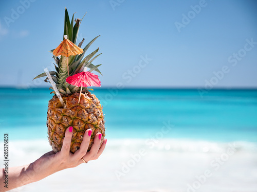 Fototapeta Naklejka Na Ścianę i Meble -  Sweet pineapple cocktail in female hand with caribbean beach background