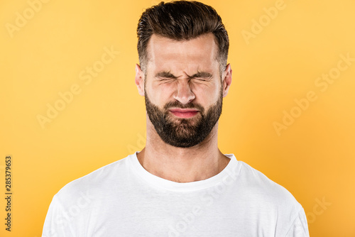 scared handsome man in white t-shirt squinting isolated on yellow
