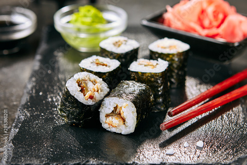 Macro shot of eel hosomaki sushi on natural black slate plate background with selective focus. Thin small unagi maki sushi rolls with rice, eel and nori closeup
