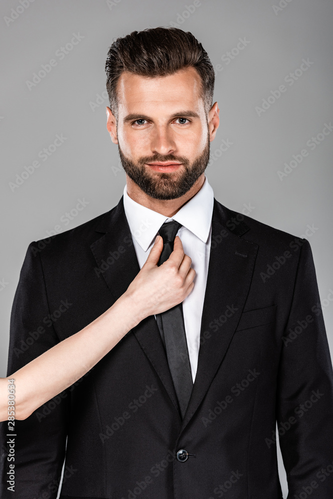 woman tying tie on successful businessman in black suit isolated on grey woman tying tie on successful businessman in black suit isolated on grey
