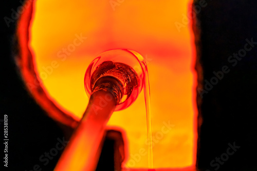 Fotografie Glass blower working on a bubble of melted glass on a rod by heating it up in a