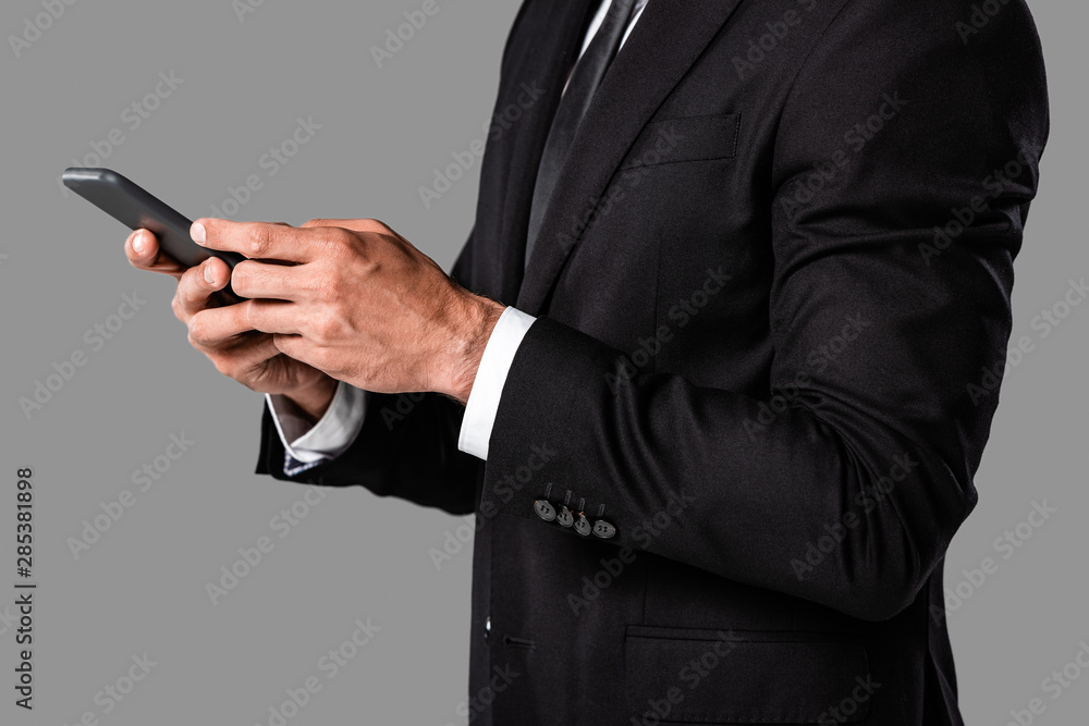 partial view of businessman in black suit using smartphone isolated on grey partial view of businessman in black suit using smartphone isolated on grey