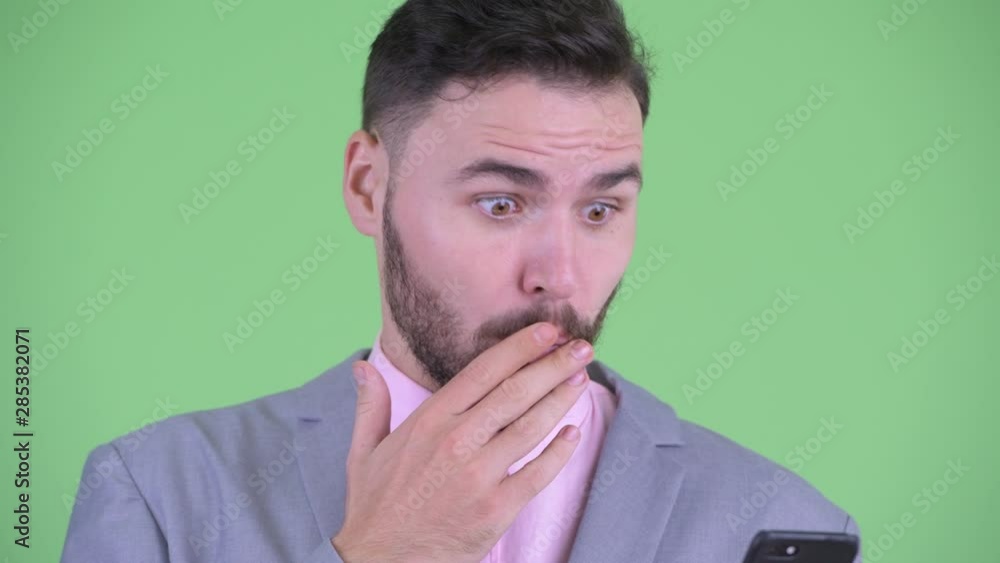 Face of happy young bearded businessman using phone and looking surprised Face of happy young bearded businessman using phone and looking surprised