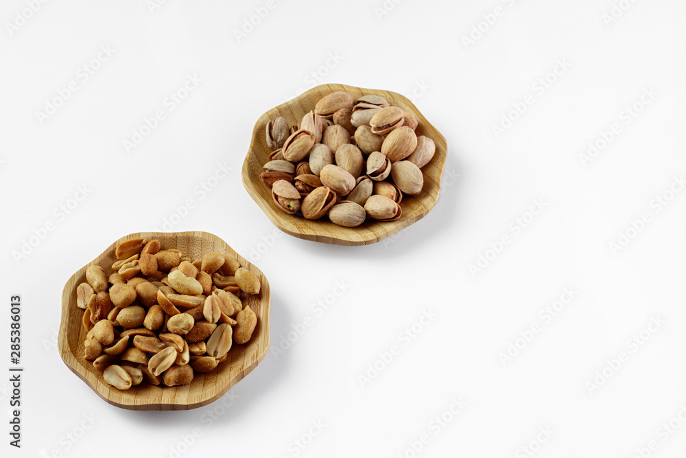 wood plates of salted peanuts and pistachios on white background. snack to beer wood plates of salted peanuts and pistachios on white background. snack to beer