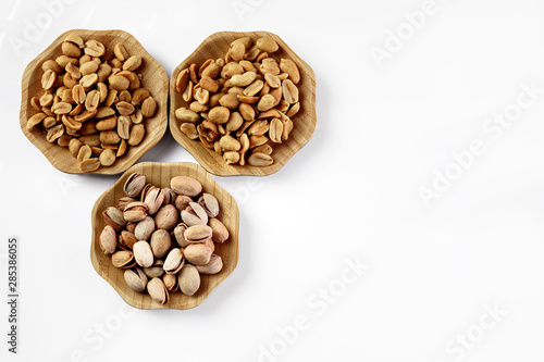 wood plates of salted peanuts and pistachios on white background. snack to beer