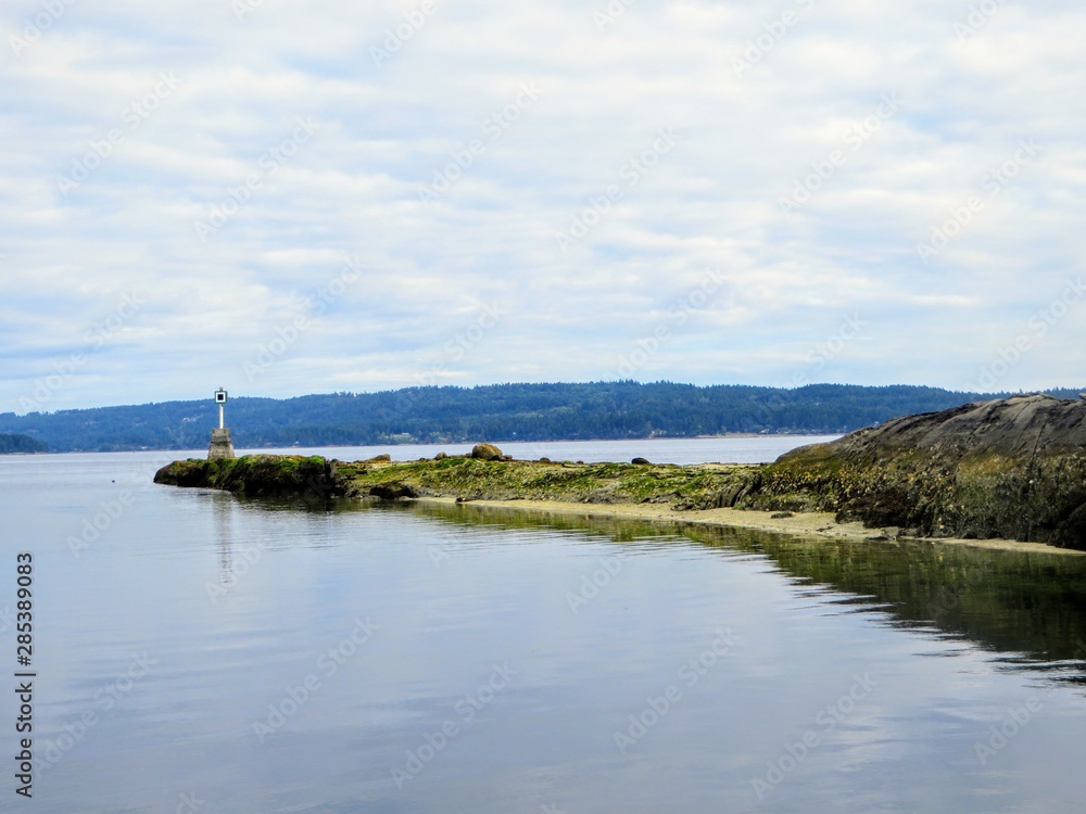 A far away view of a port hand day beacon at low tide at the end of a reef on an island.  The Port Hand Day Beacon marks the port (left) side of a channel or the location of a danger 