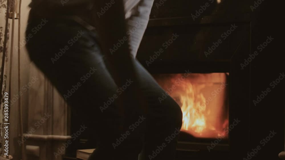 A young black-haired man reads a book by the fireplace, then closes the book, gets up and goes to bed A young black-haired man reads a book by the fireplace, then closes the book, gets up and goes to bed