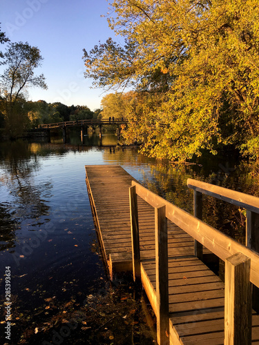 Autumn View of a Dock Extending Over the Water with the Old North Bridge in the Distance and Reflecting in the Water. Concord, MA.