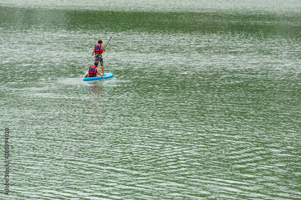 Two young guys are floating on a Board La sup surfing on the lake.