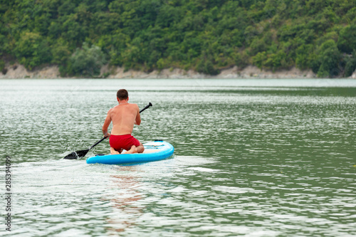 A young guy is floating on a Board La sup surfing on the lake.