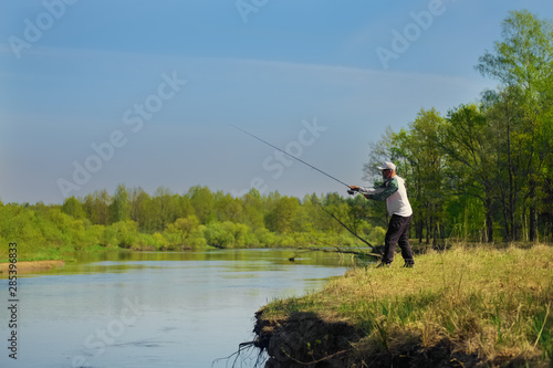 Man fish with spinning on river bank, casting lure. Outdoor weekend activity. Photo with shallow depth of field taken at wide open aperture.
