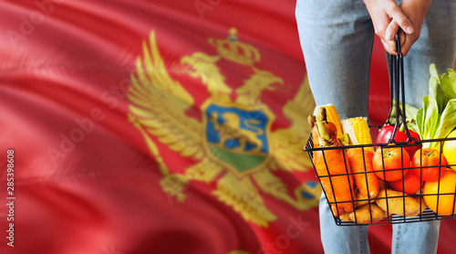 Woman is holding supermarket basket, Montenegro waving flag background. Economy concept for fresh fruits and vegetables.
