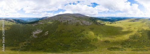 Fototapeta Naklejka Na Ścianę i Meble -  360 degree panoramic aerial view in the wild with green fields and grass and a high mountain with a rocky peak on a warm summer day with white clouds and blue sky with high detail. 3d tour