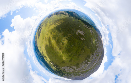 Aerial view of planet in the form of a nutlet with image of nature and picturesque landscapes near a mountain with a rocky peak on a summer day with white clouds and blue sky. 