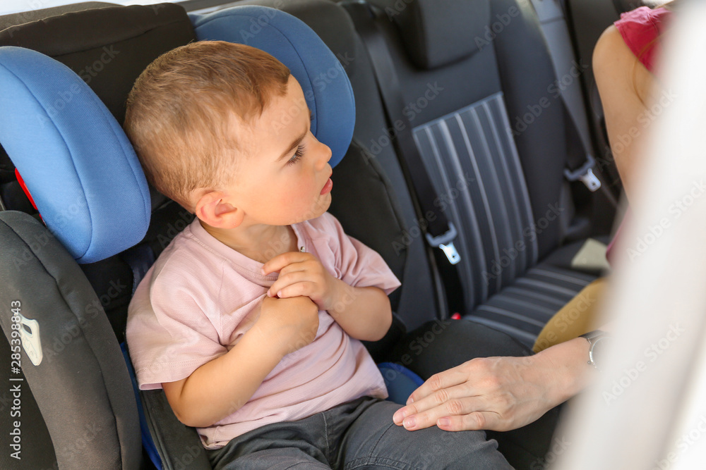 Mother buckling her little son in car seat Mother buckling her little son in car seat