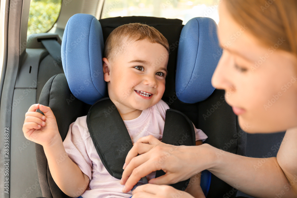 Mother buckling her little son in car seat