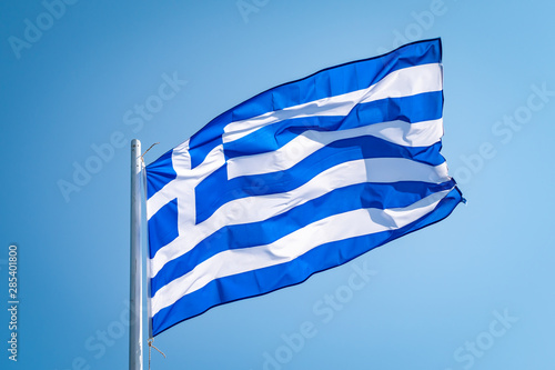 Flag of Greece waving in the wind in front of blue sky.