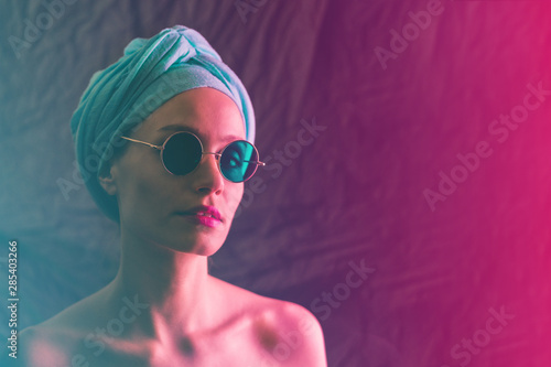 Portrait of girl in neon light, dressed in blue turban on her head and green glasses.