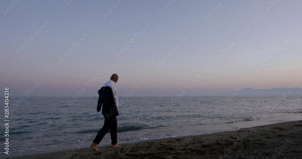 Happy successful man walking in the evening on the beach in a business suit, slow motion Happy successful man walking in the evening on the beach in a business suit, slow motion