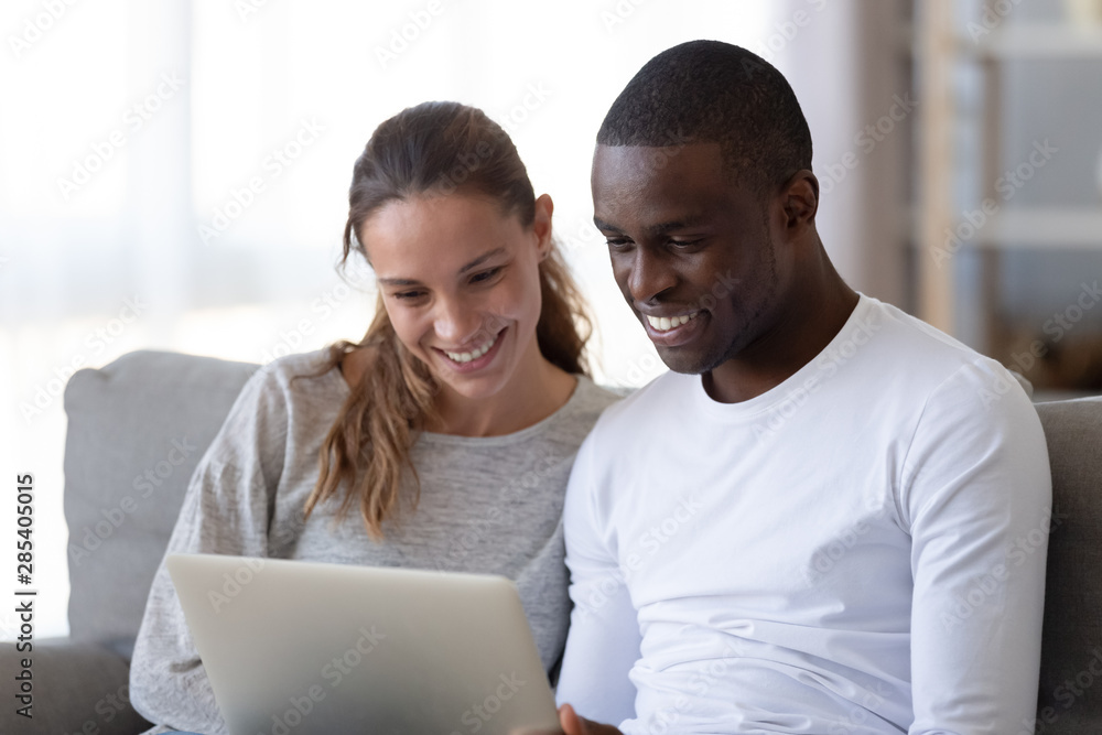 Happy mixed race young couple using laptop looking at screen Happy mixed race young couple using laptop looking at screen