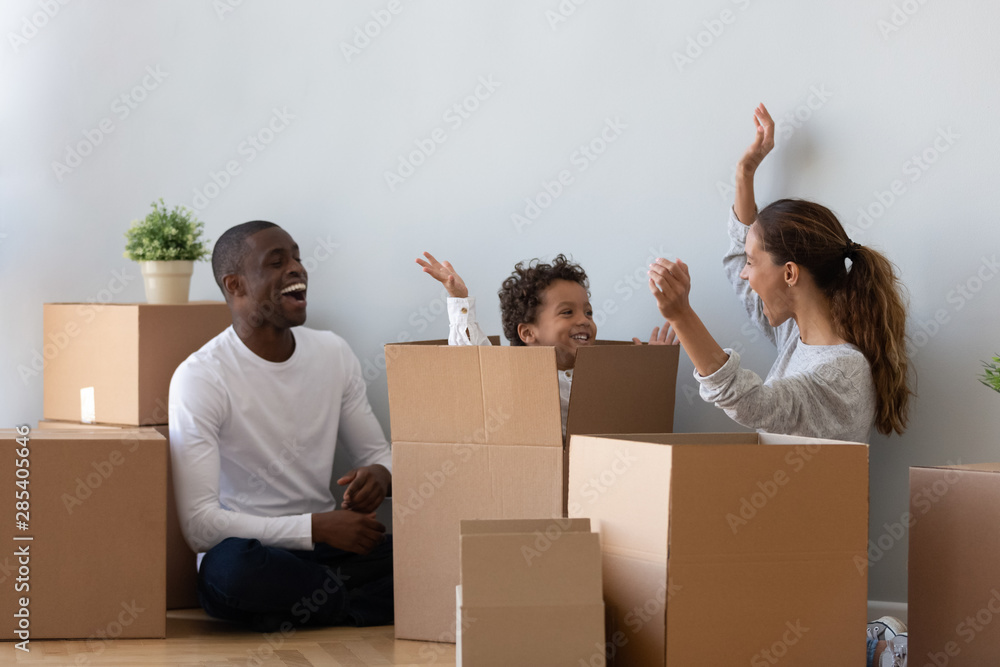 Happy mixed ethnicity family playing on moving day unpacking boxes - obrazy, fototapety, plakaty 
