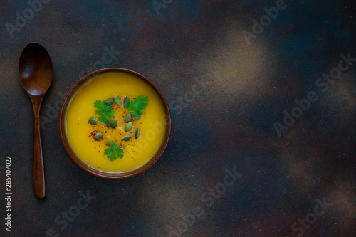 Roasted butternut squash cream soup with pumpkin seeds,pumpkin slices on dark background,copy space,top view