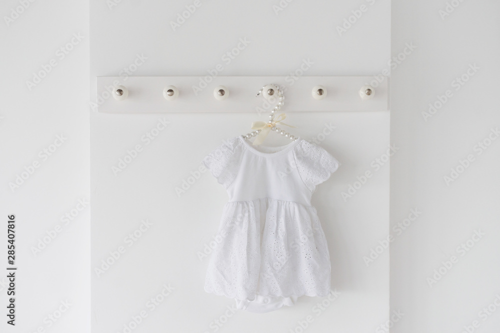 A newborn white dress on a hanger in a light room. Waiting a baby concept. A newborn white dress on a hanger in a light room. Waiting a baby concept.