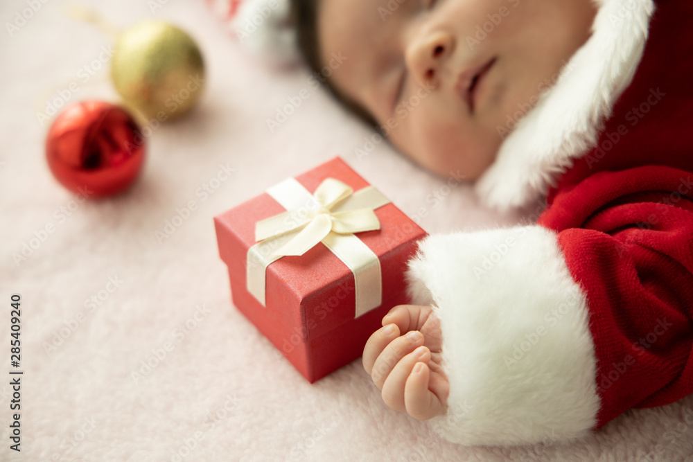 Asian baby newborn on Santa claus uniform sleeping with red box present and red hat Asian baby newborn on Santa claus uniform sleeping with red box present and red hat